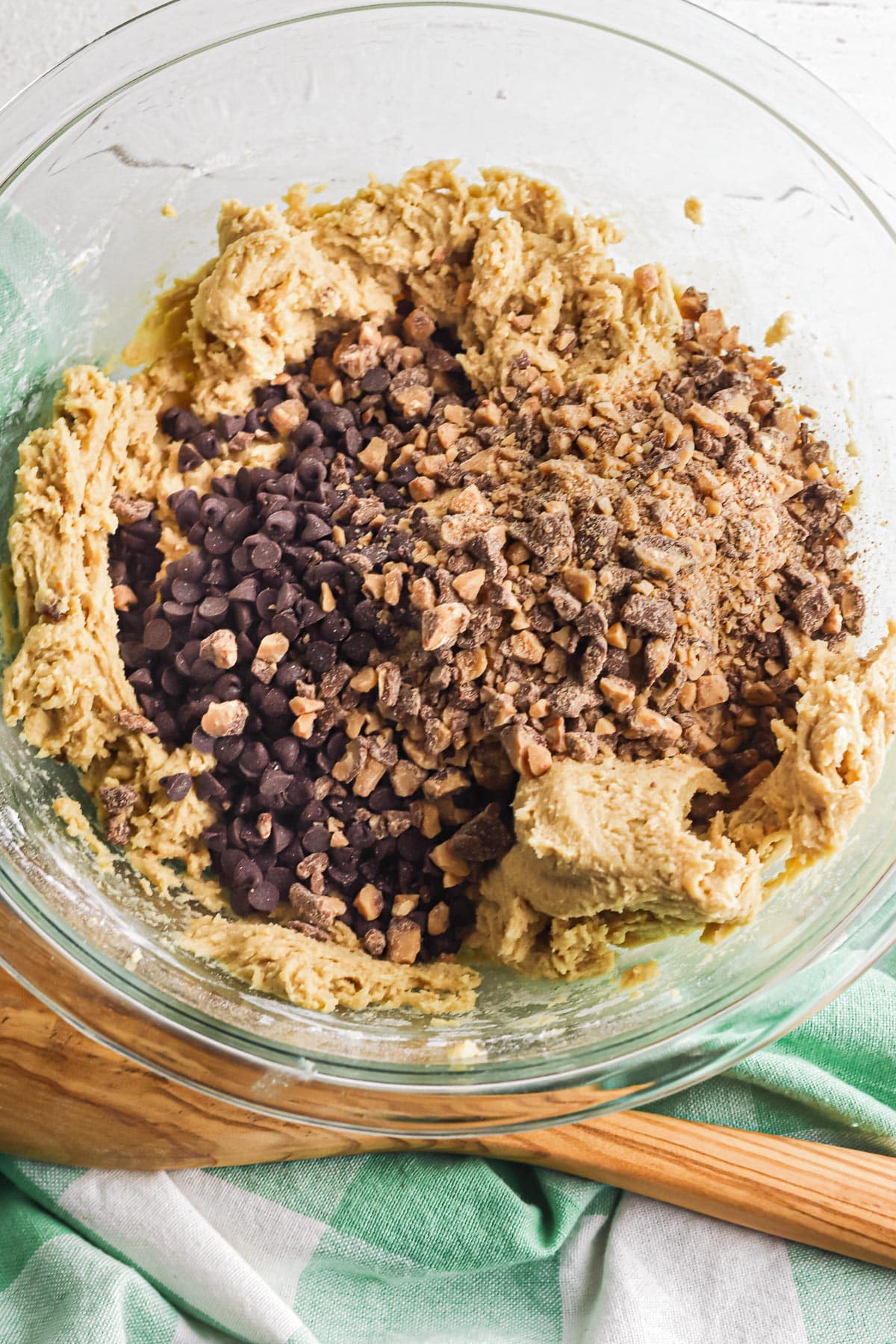 Chocolate chips and toffee bits being mixed into a cookie dough in a mixing bow.