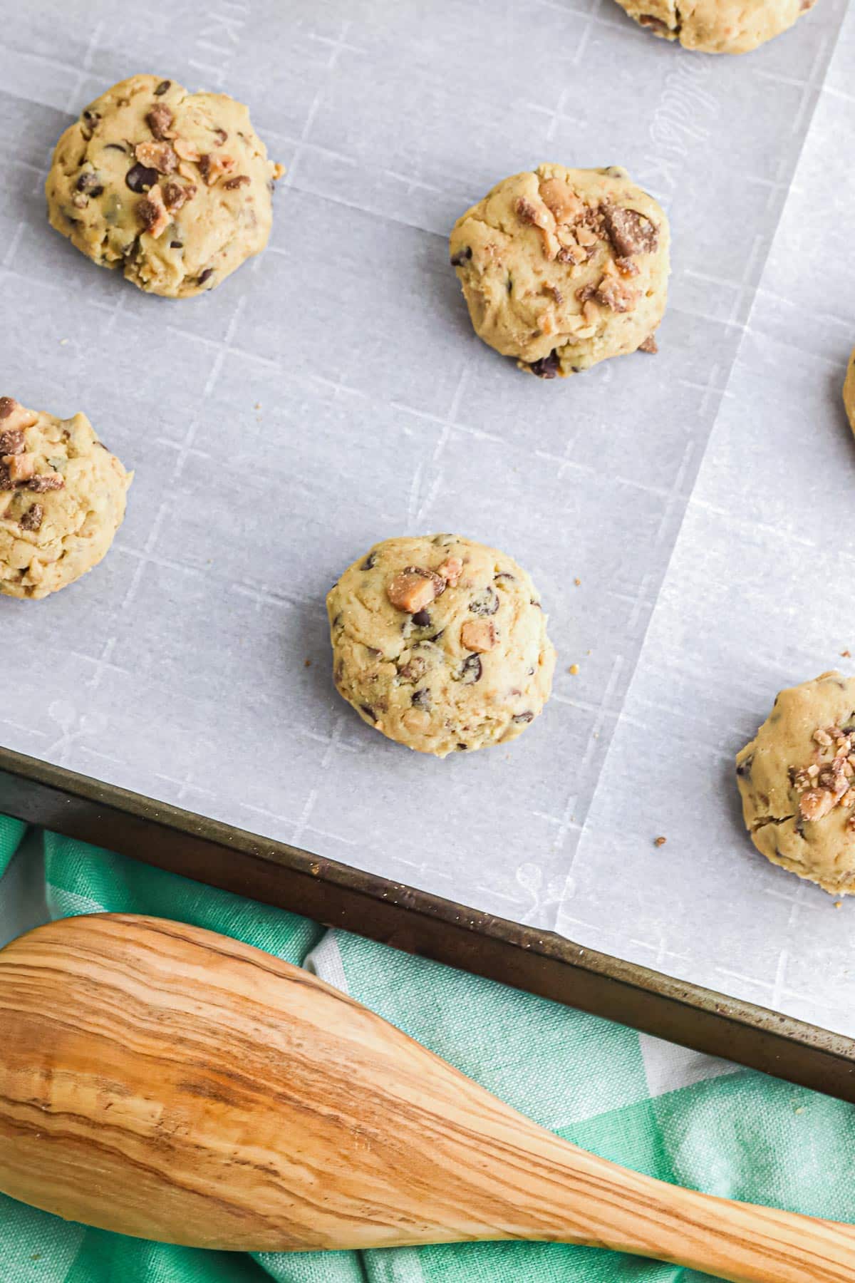 Unbaked cookies with chocolate chips and toffee bits on parchment lined pan.
