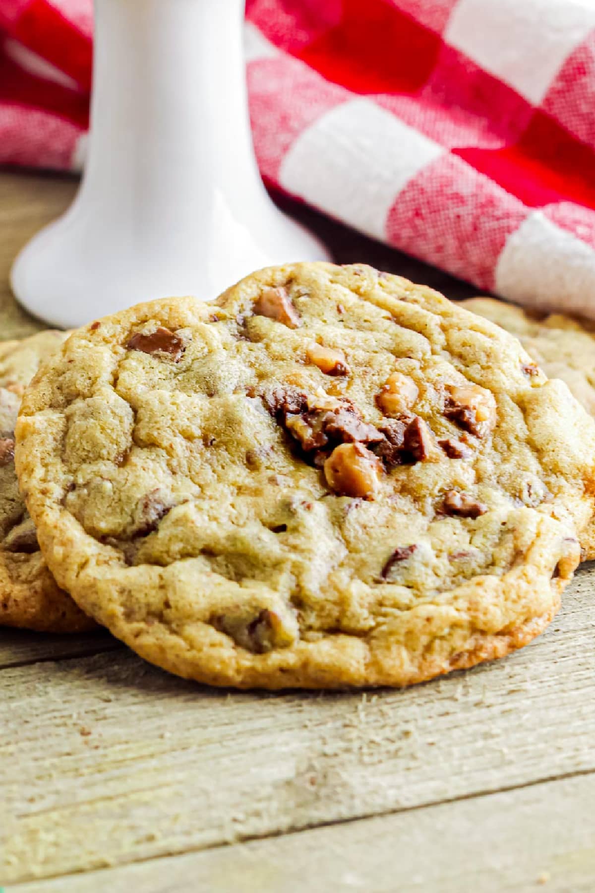 A close-up of a chocolate chip toffee cookie on a wooden table.