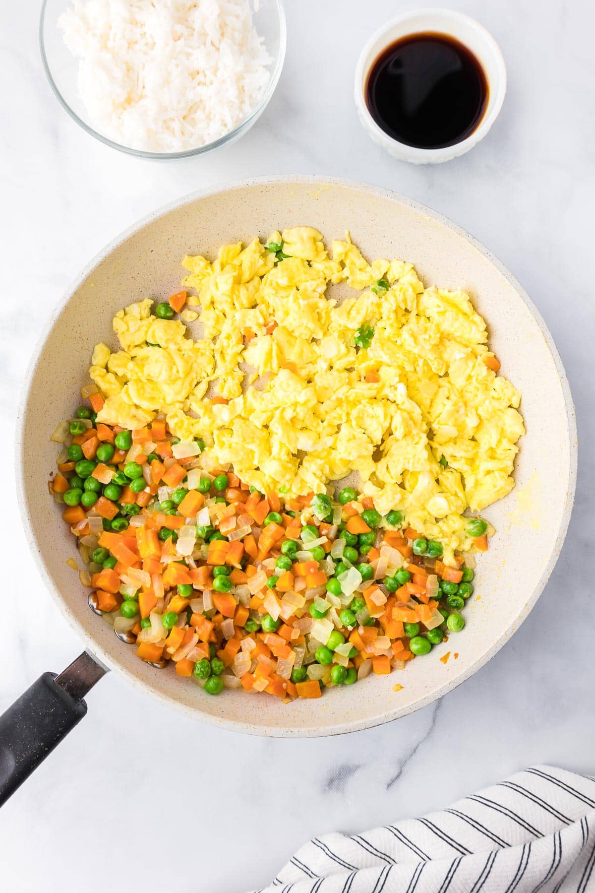 A frying pan with scrambled eggs on one side and a mixture of diced vegetables on the other for fried rice.