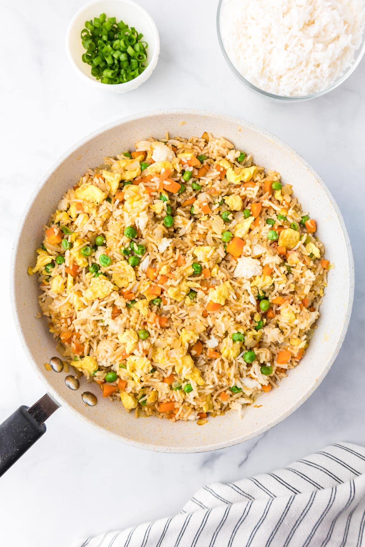 A skillet filled with fried rice containing peas, carrots, and scrambled eggs