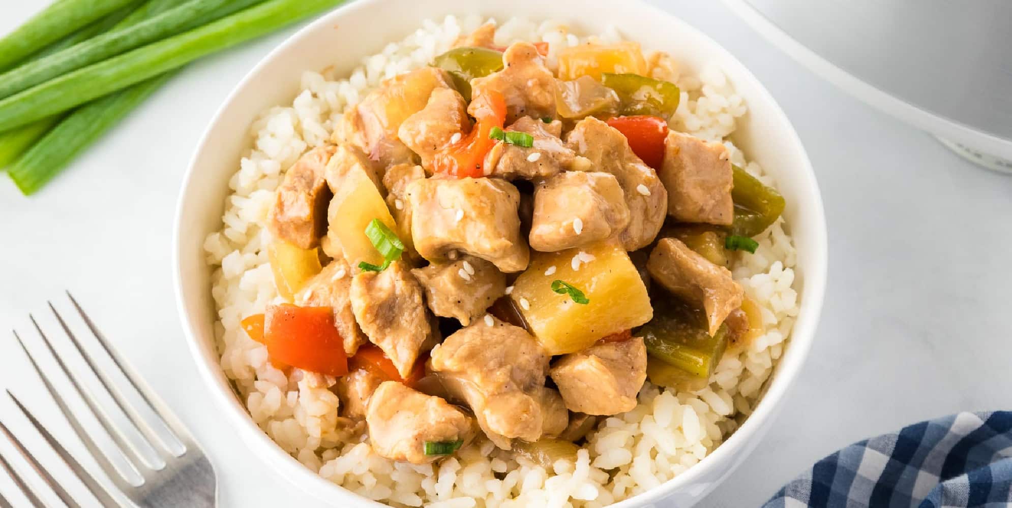 Wide view of a bowl of sweet and sour pork with pineapple and peppers on top of rice.