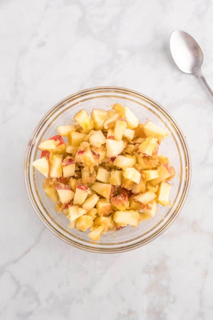 A glass bowl filled with diced apples mixed with melted butter and brown sugar for apple french toast casserole.