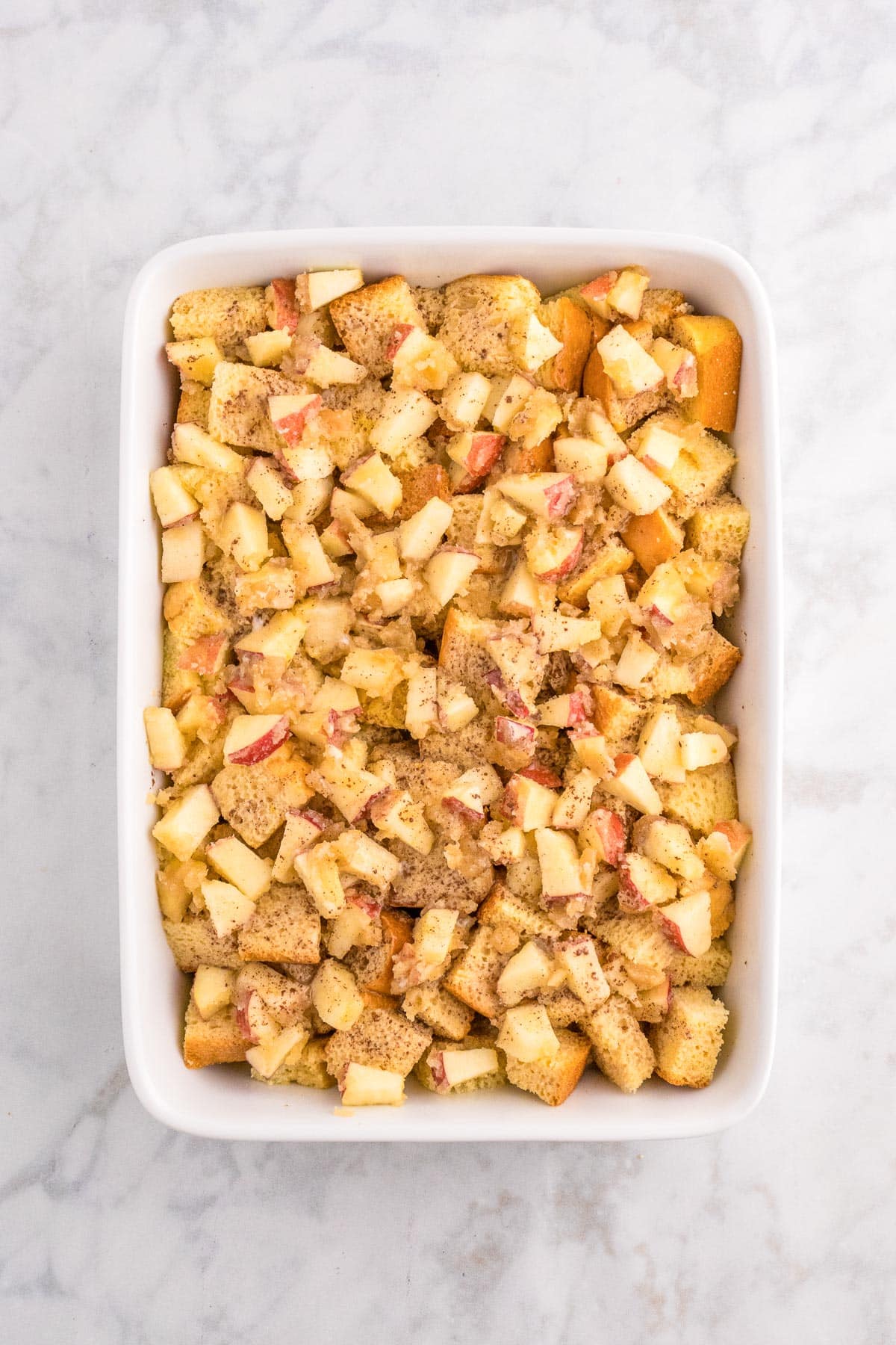 A large baking dish full of cubed bread with an apple butter brown sugar mixture and the egg custard mixed in for apple french toast casserole.