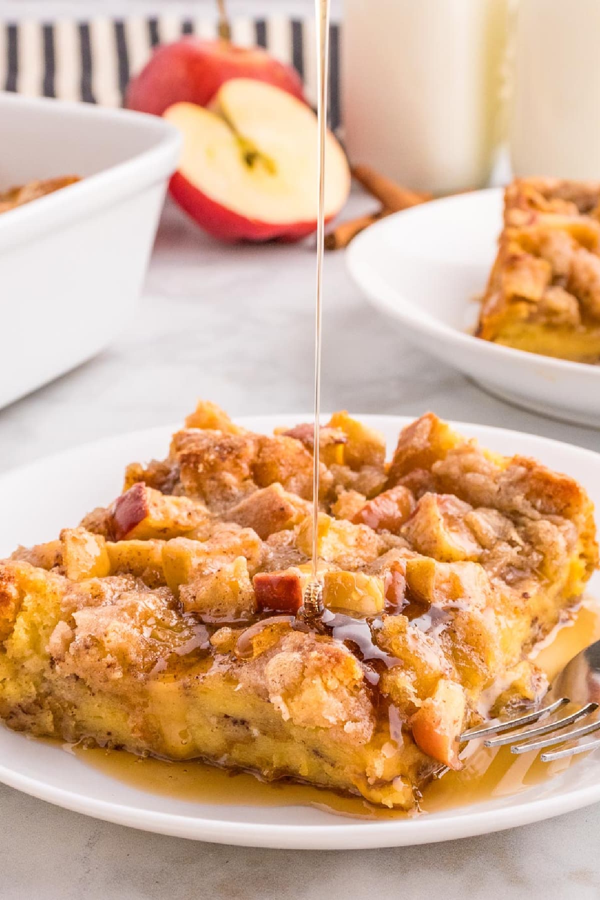 A piece of baked apple French toast casserole on a plate with maple syrup being drizzled on top.