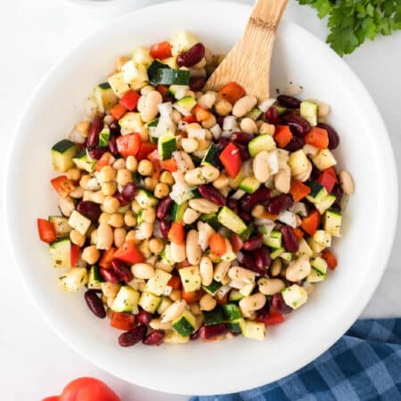 A white bowl containing a mixed bean chickpea and vegetable salad with a variety mixed together.