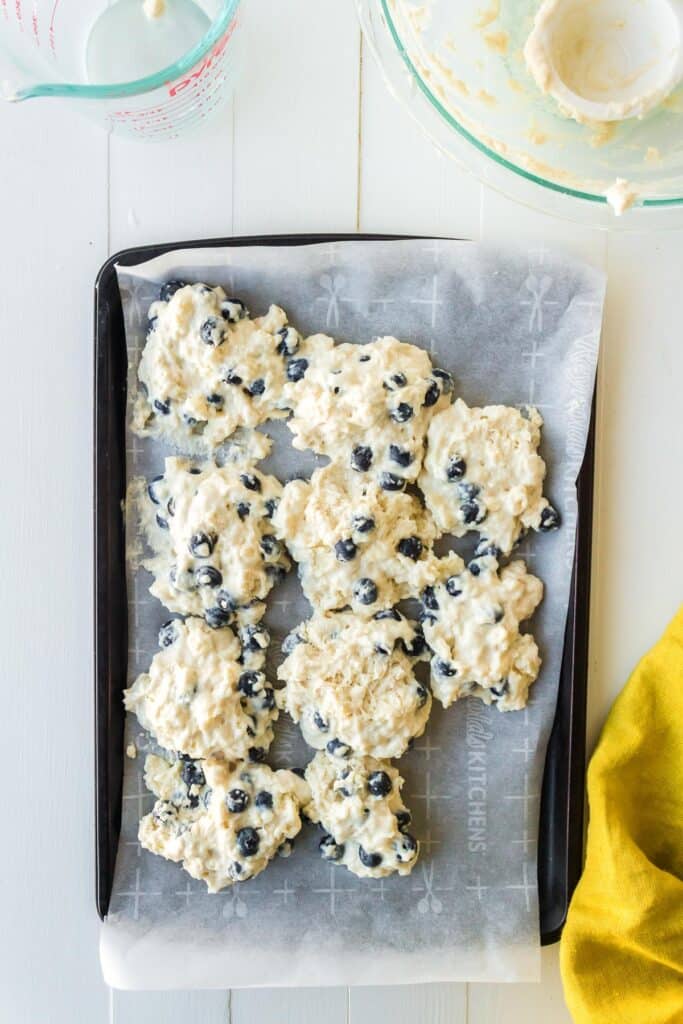 A baking tray lined with parchment paper full of 10 blueberry biscuits before baking.