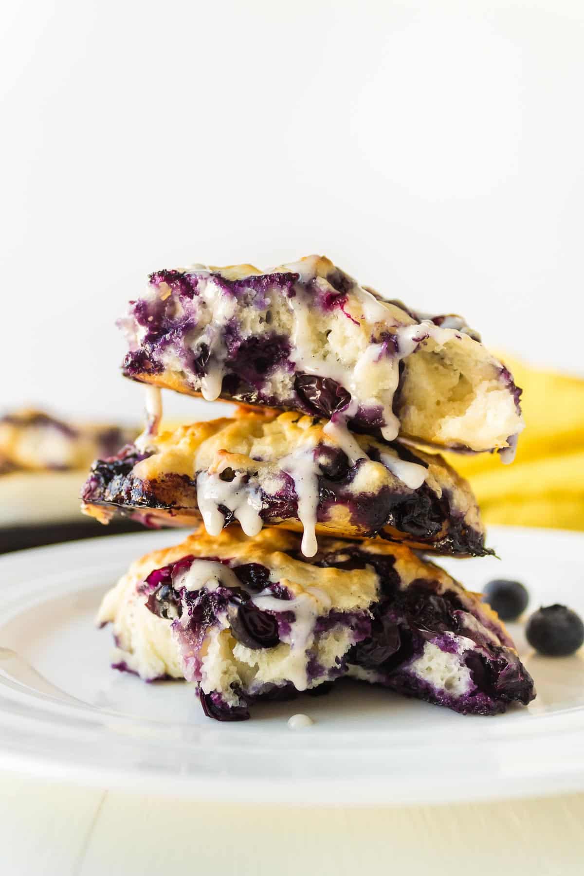 A stack of blueberry biscuits on a plate drizzled with white vanilla glaze.