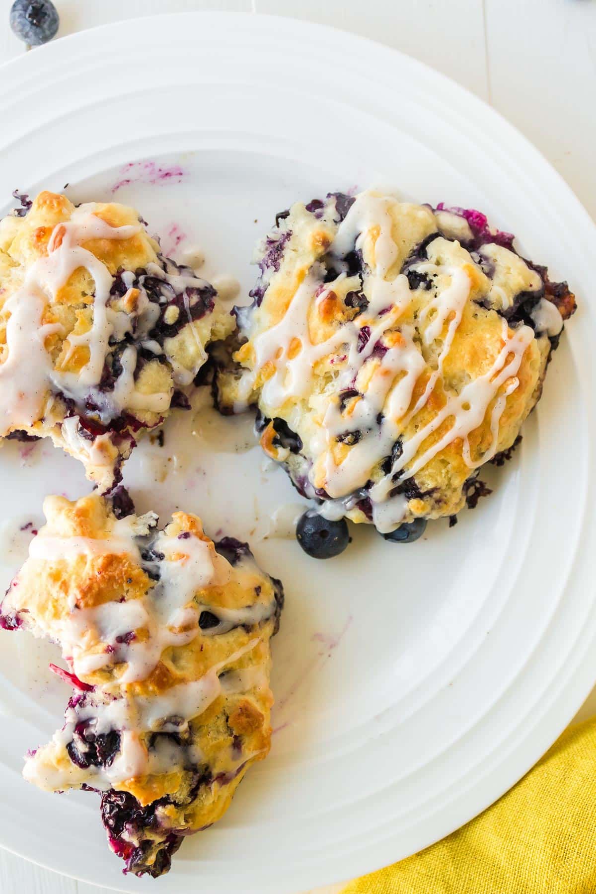 Three blueberry muffins with white glaze drizzle on a white plate.