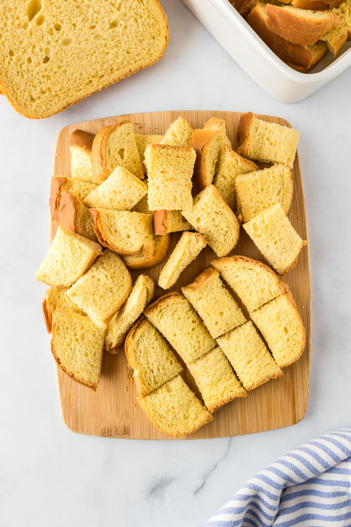 A wooden cutting board holding brioche bread being cut into chunks.