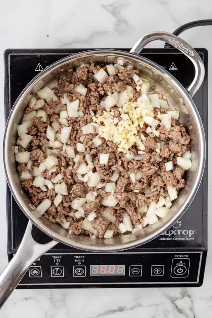 Cooked ground beef with onion and garlic being added on a burner.