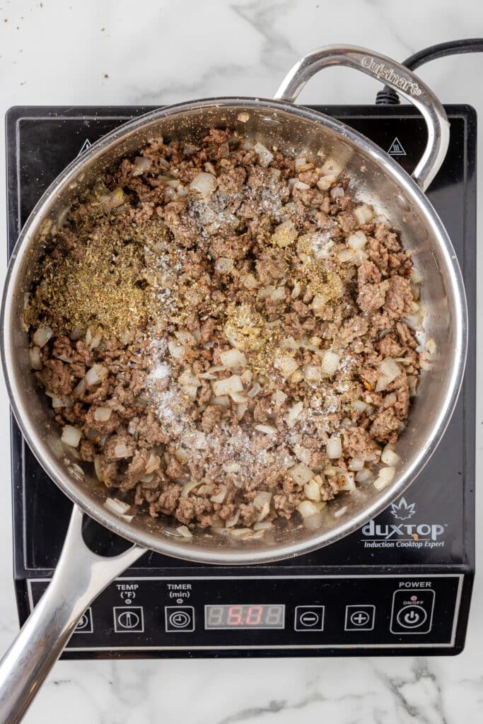 Cooked ground beef with onions and spices being mixed together for cheesy hamburger helper pasta.