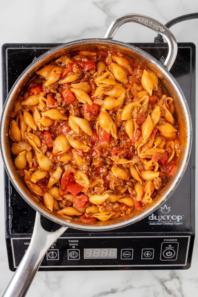 A stovetop pan filled with cooked cheesy hamburger helper on a burner.