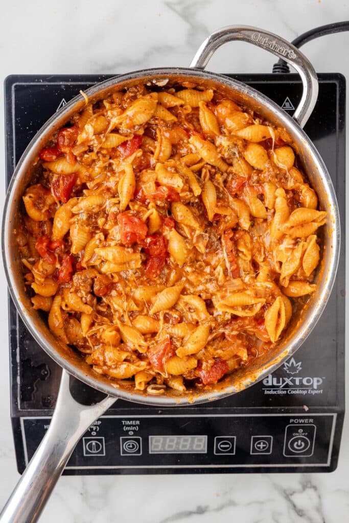 A pan of cheesy homemade hamburger helper after it is finished cooking on a burner.