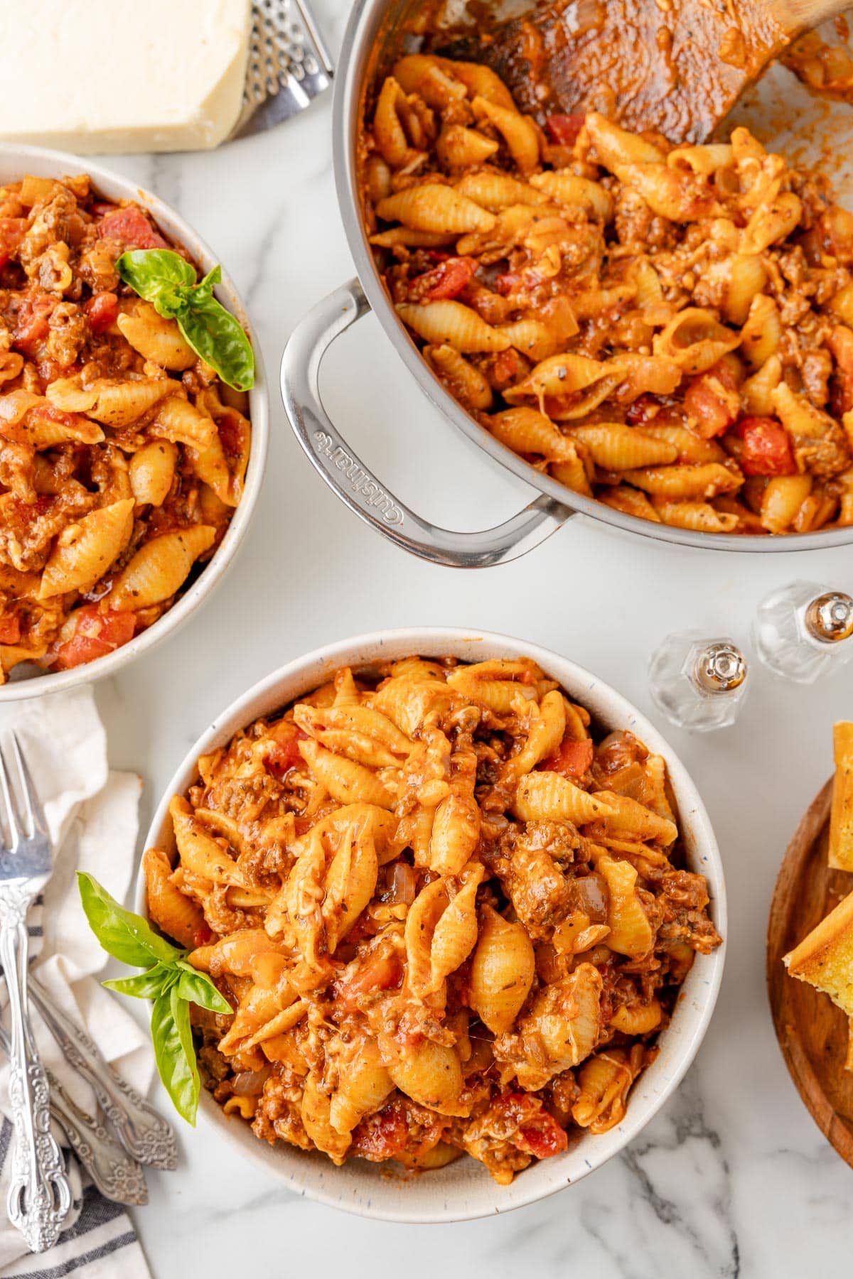 Two bowls of cheesy homemade hamburger helper pasta with a skillet full of more pasta on the table nearby.