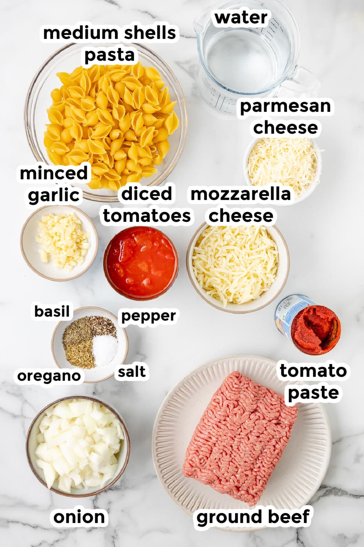 Ingredients for cheesy hamburger helper with shells in bowls with text title labels from overhead on a counter.