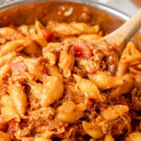 A wooden spoon stirring a skillet filled with cheesy homemade hamburger helper in a pan.