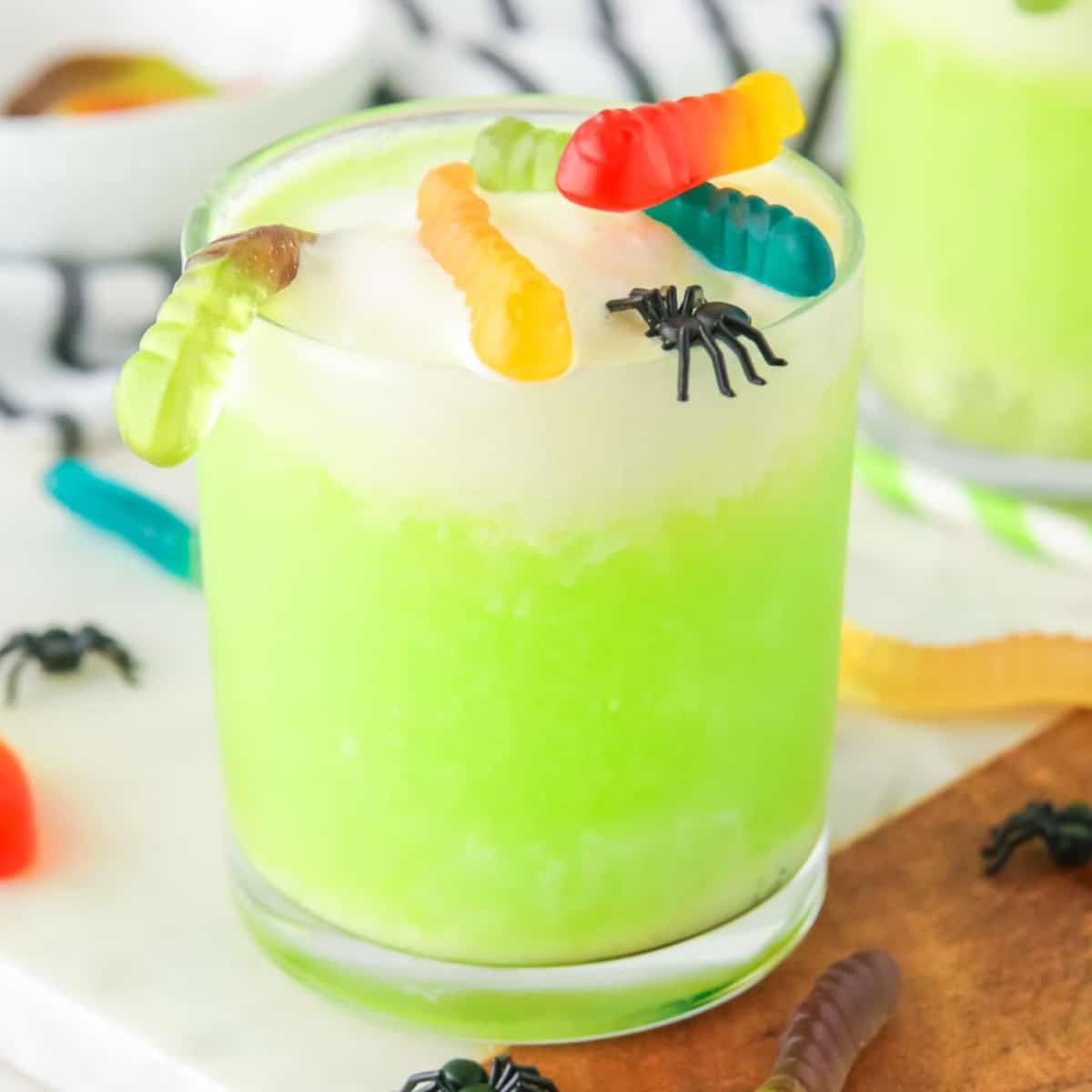 A square view of a glass of green Halloween punch topped with gummy worms and gummy bugs.