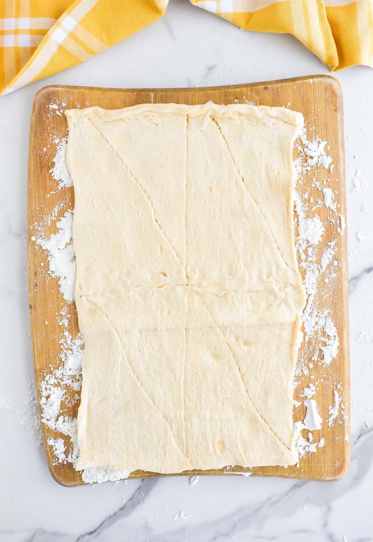 Unrolled crescent roll dough on a wooden cutting board dusted with flour.