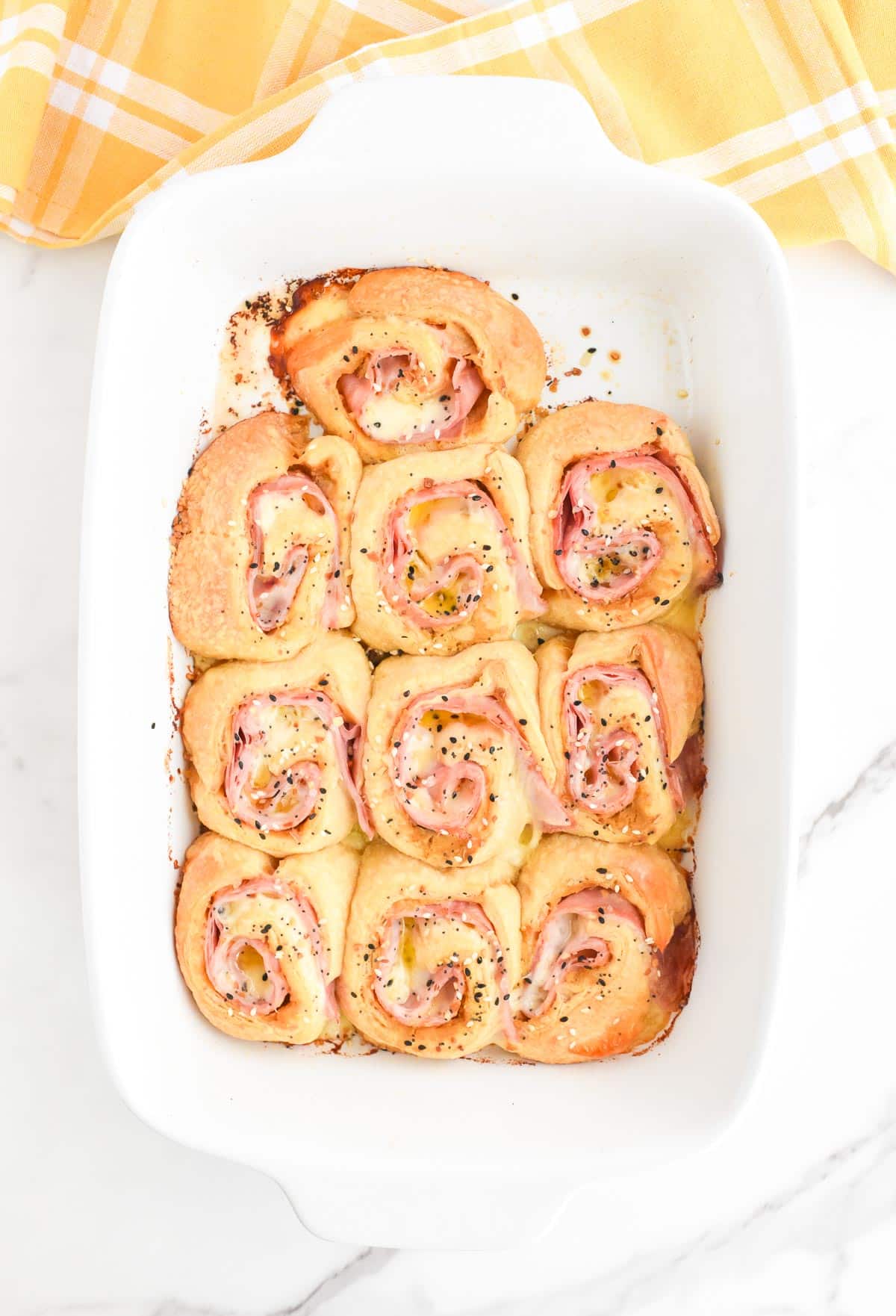 A baking dish full of ham and cheese pinwheels baked until golden brown and topped with everything bagel seasoning.