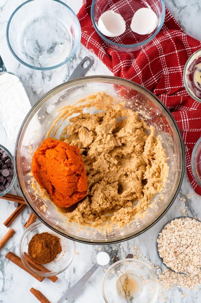 A mixing bowl with pumpkin oatmeal cookie dough with pumpkin being mixed into the dough.