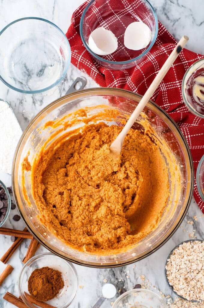 A glass bowl with a pumpkin oatmeal cookie dough after adding pumpkin.