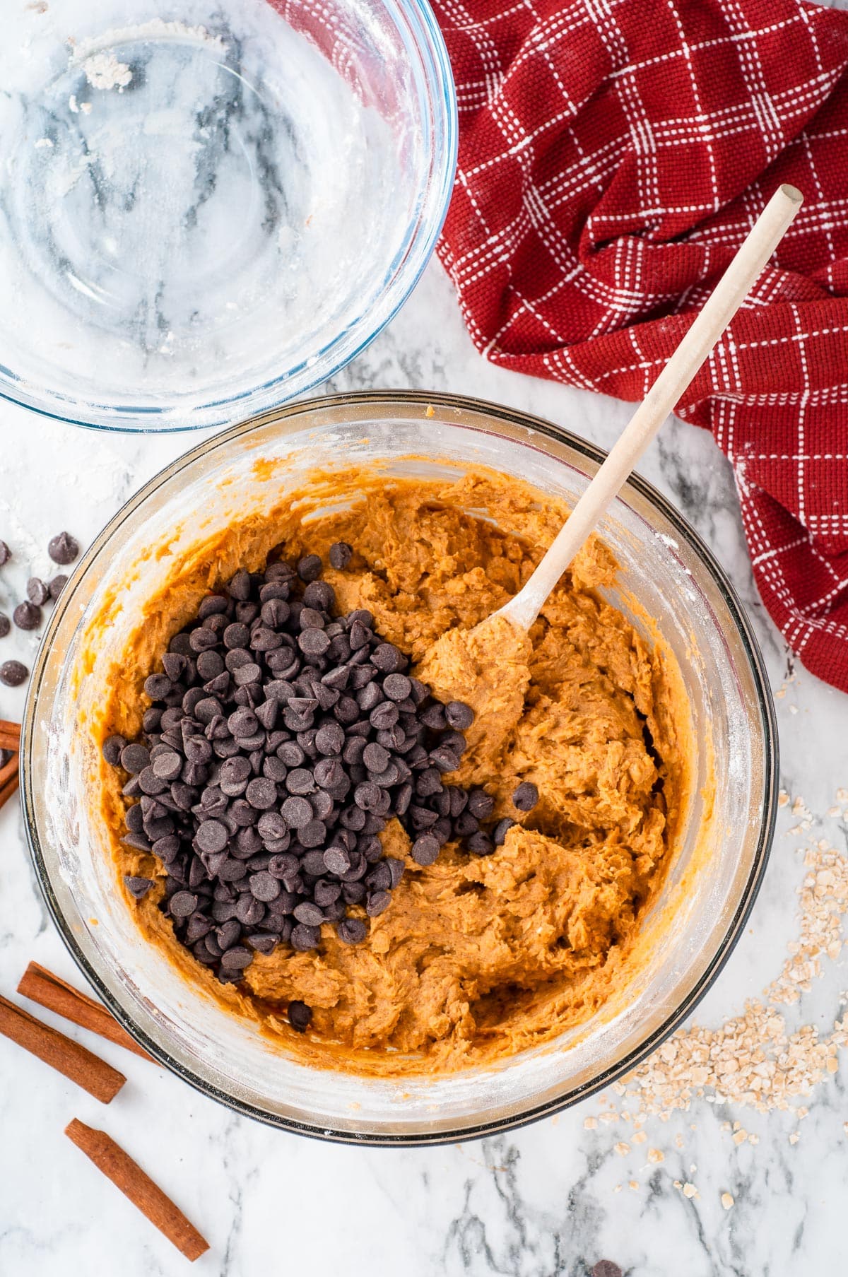 A glass bowl filled with pumpkin oatmeal cookie dough with a wooden spoon folding in chocolate chips.