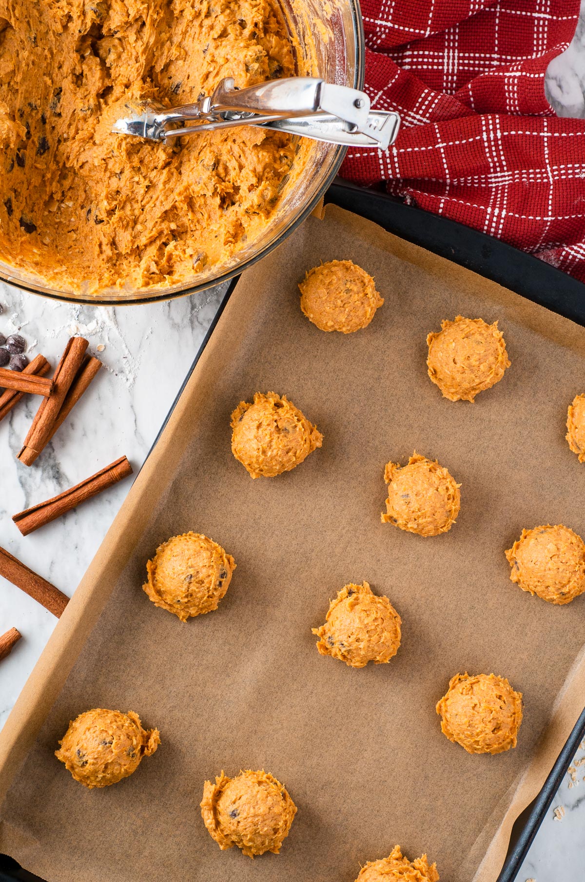 Oatmeal pumpkin cookie dough scoops on a parchment-lined baking sheet next to a mixing bowl from above.