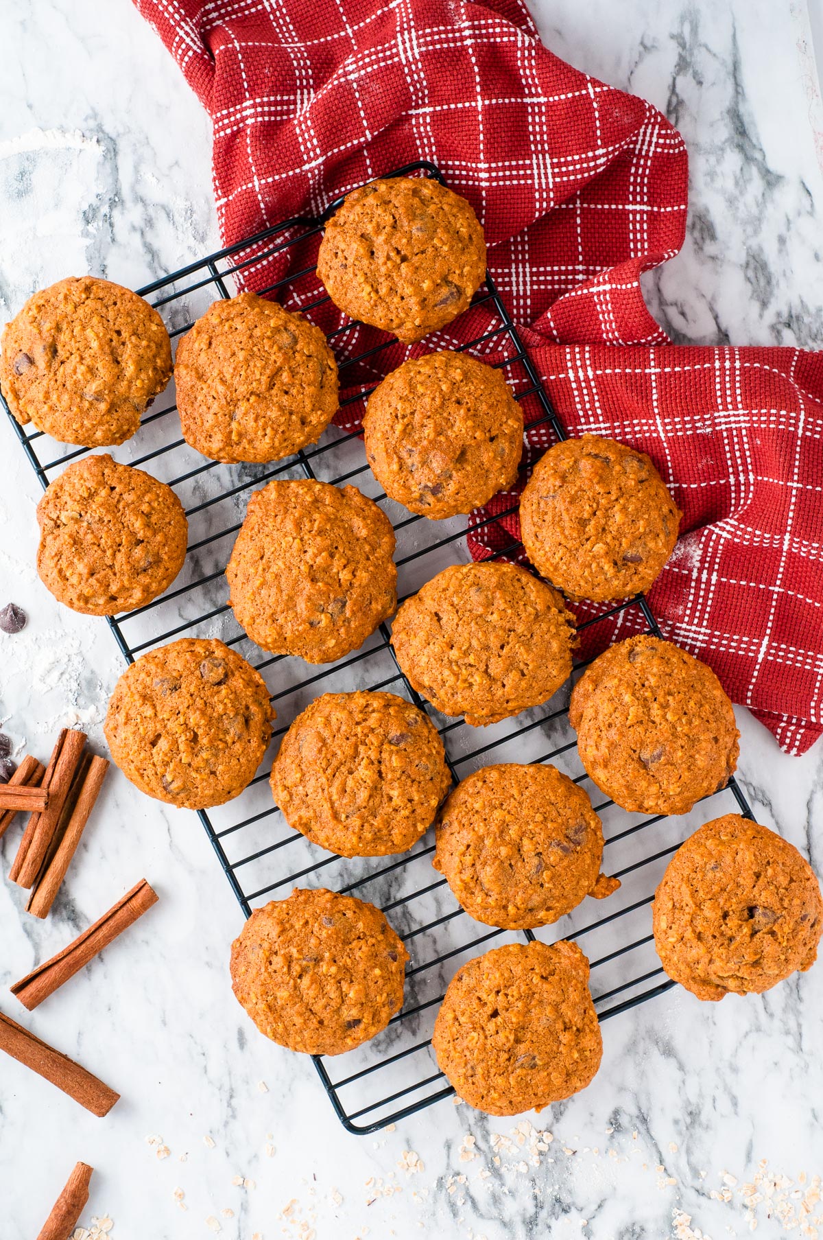 A cooling rack with sixteen pumpkin oatmeal cookies on a table.