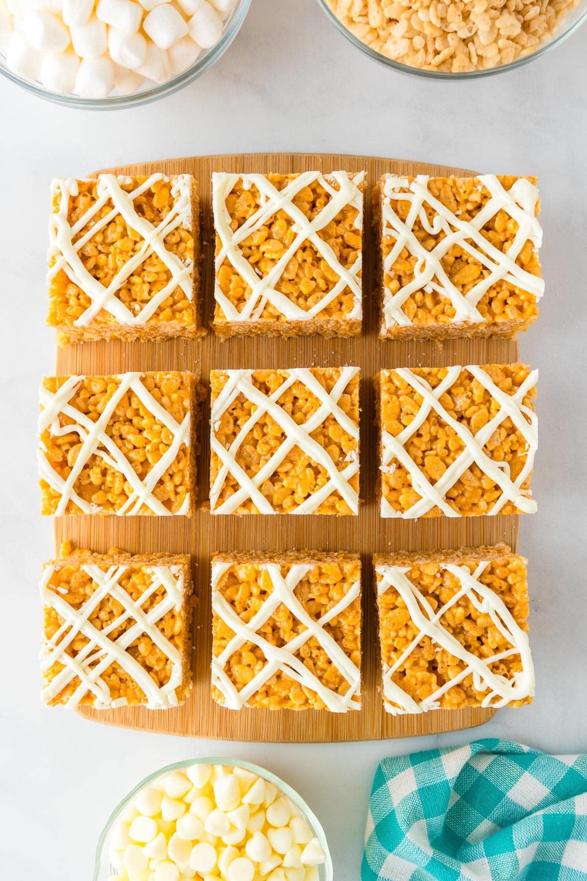 Nine sliced Pumpkin Spice rice crispy treats with white chocolate drizzle on a wooden cutting board.