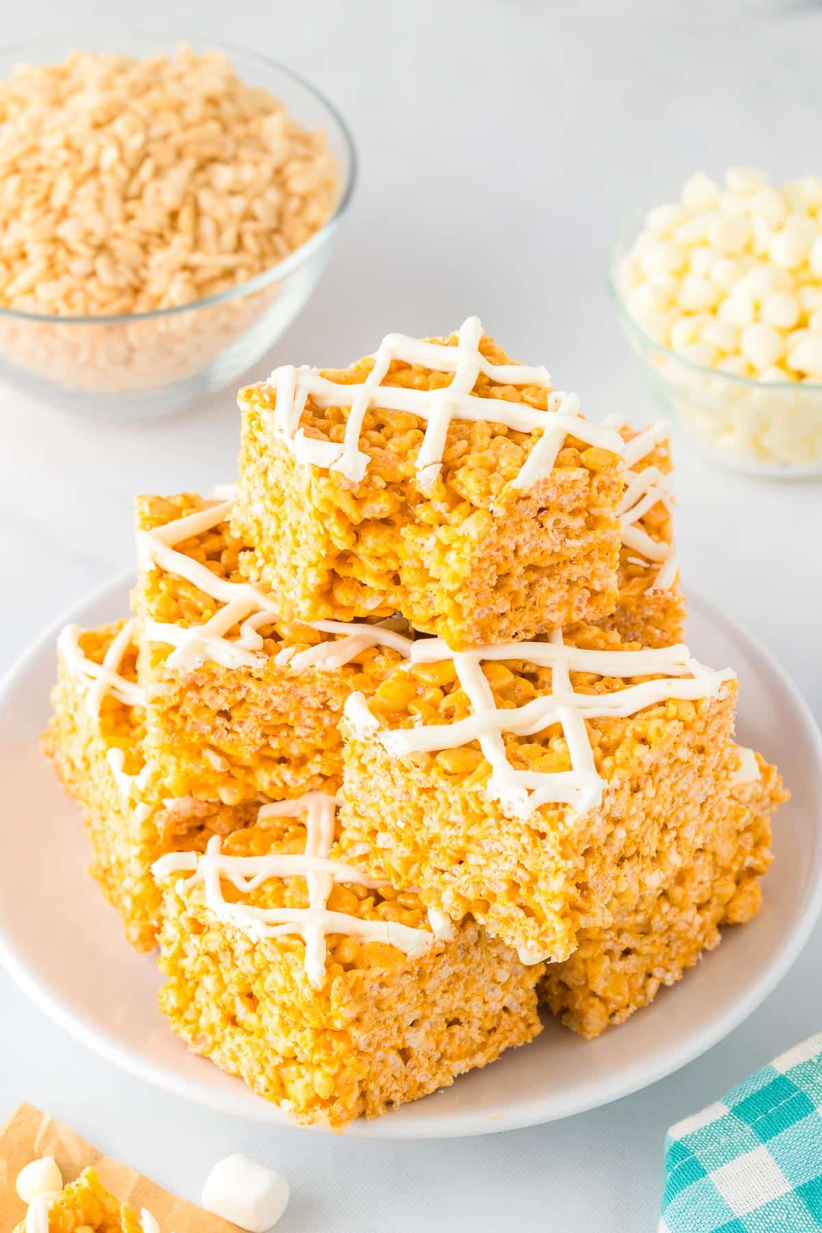 A plate stacked with square pumpkin spice rice crispy treats drizzled with white chocolate with the top piece missing a bite.