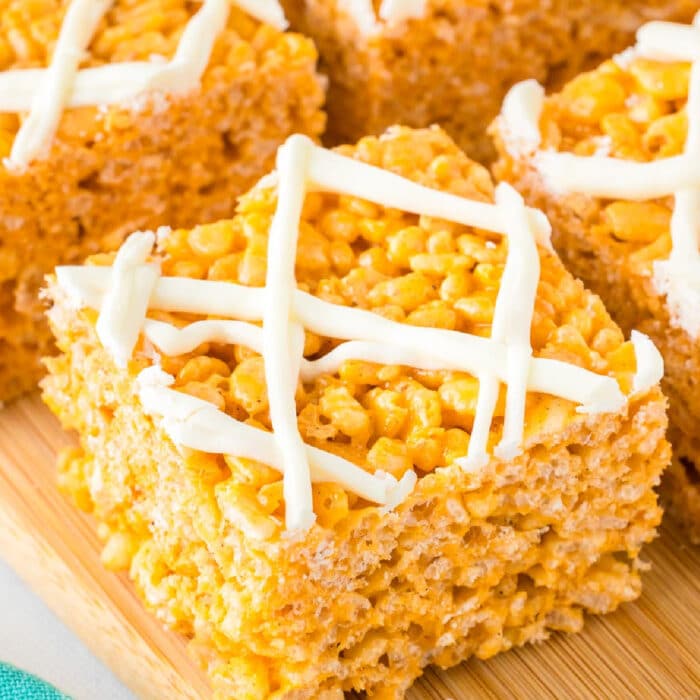 Close-up of several Pumpkin spice rice crispy treats topped with white chocolate on a cutting board close up on the front piece.