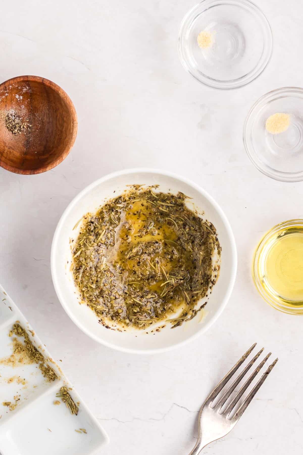 A bowl containing a mix of dried spices and herbs with melted butter mixed together with more small bowls nearby.