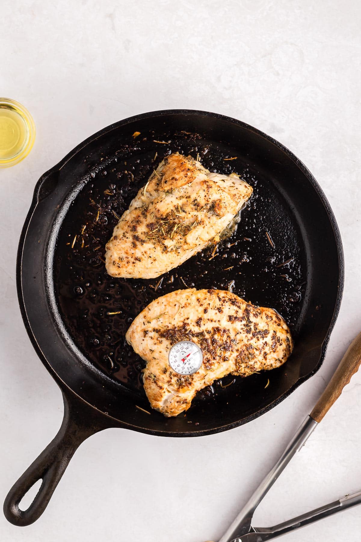 Two seasoned turkey tenderloins cooking in a black cast-iron skillet, one with a meat thermometer in it.