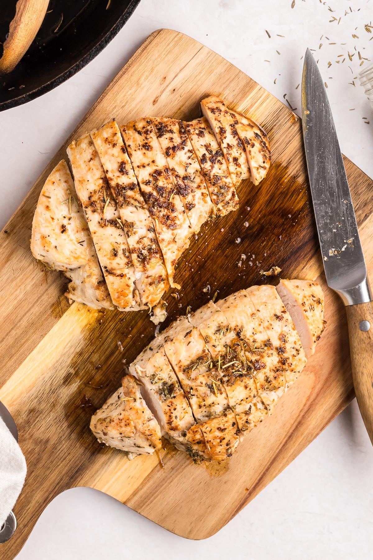 Two pieces of sliced roasted turkey tenderloin on a cutting board next to a knife.