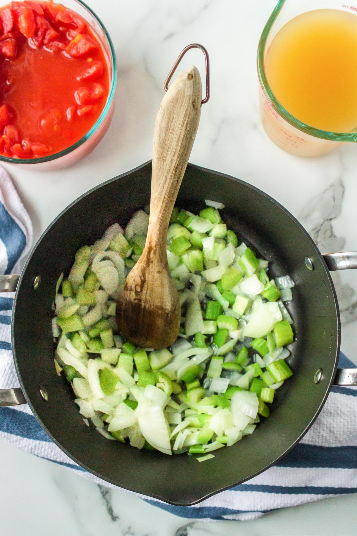 A cooking pot with chopped onions and celery being stirred and cooked with a wooden spoon.