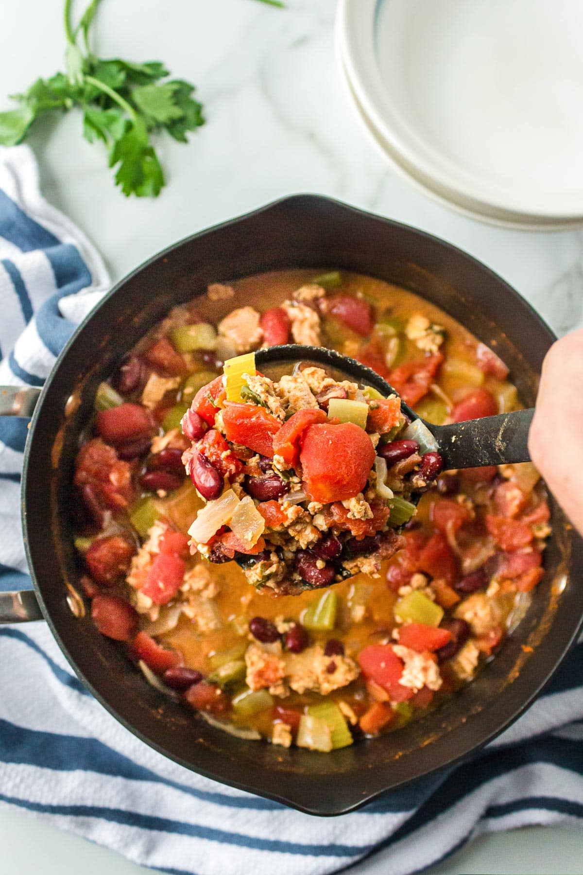 A hand holding a ladle filled with turkey chili being scooped from a pot.