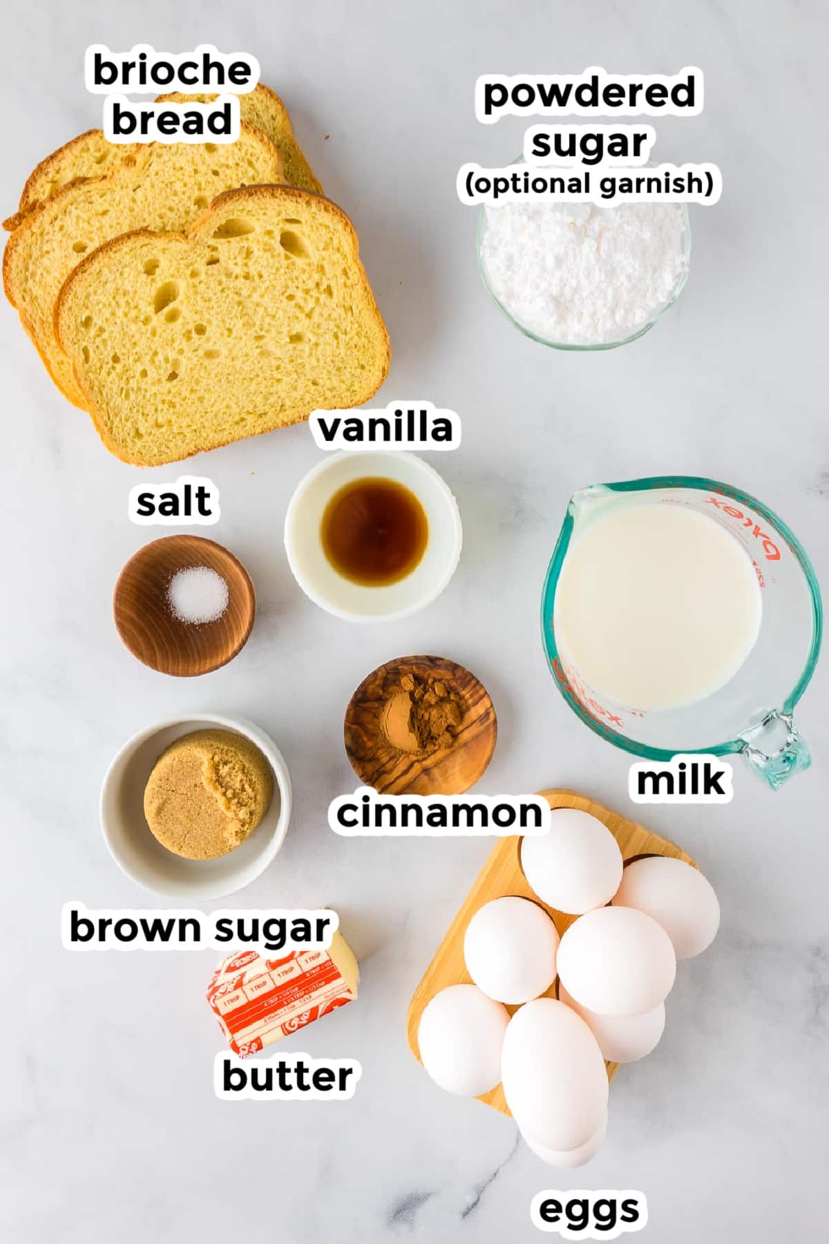 Ingredients on a table in bowls for making brioche french toast casserole with text ingredient labels.