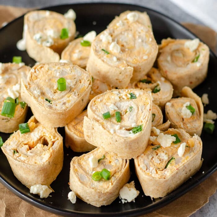 A plate of rolled tortillas filled buffalo chicken and cheese, sprinkled with chopped green onions and crumbled blue cheese.