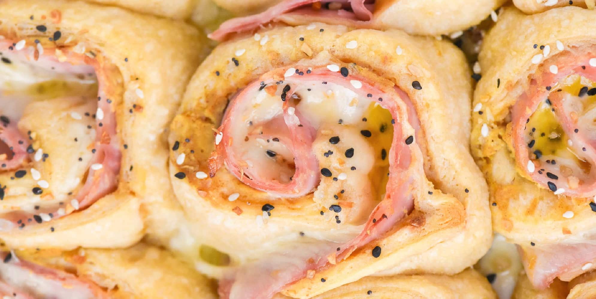 Wide view close-up of ham and cheese pinwheel rolls topped with sesame and poppy seeds close up in the pan.