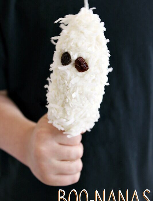 A hand holding a banana covered with coconut shreds, decorated to look like a ghost.