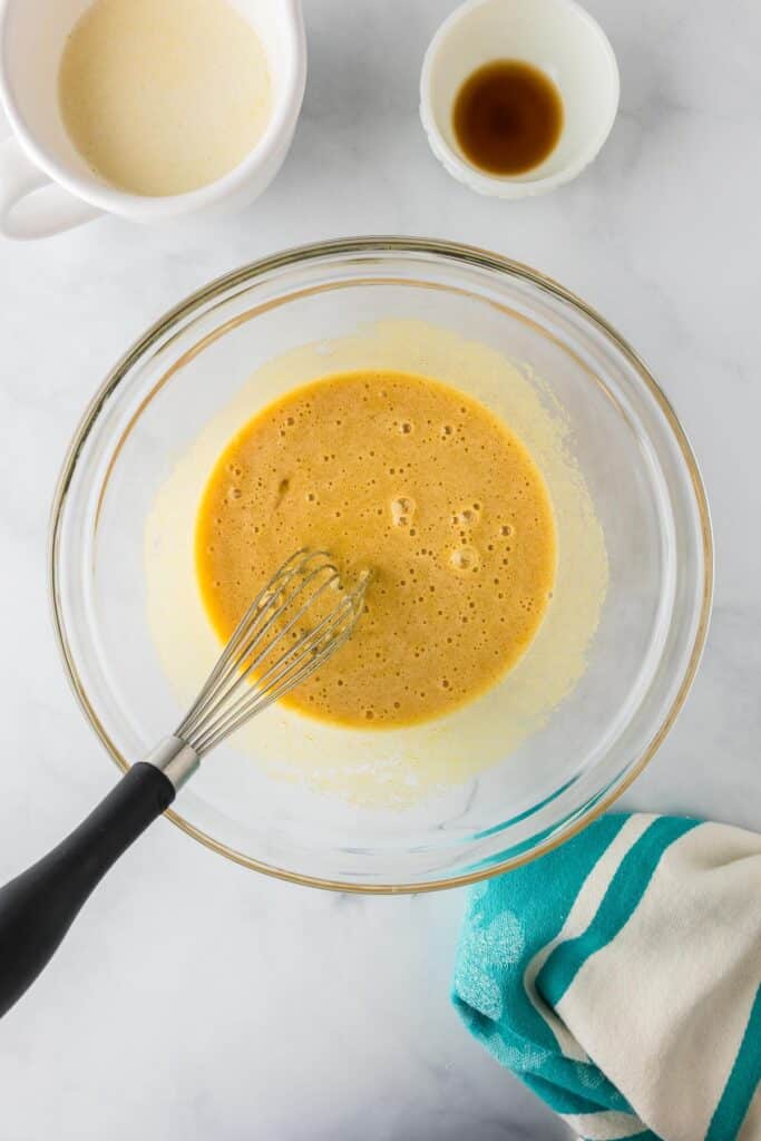 A whisk in a glass bowl mixing a yellow wet batter mixture for andes mint brownies before adding the dry ingredients.