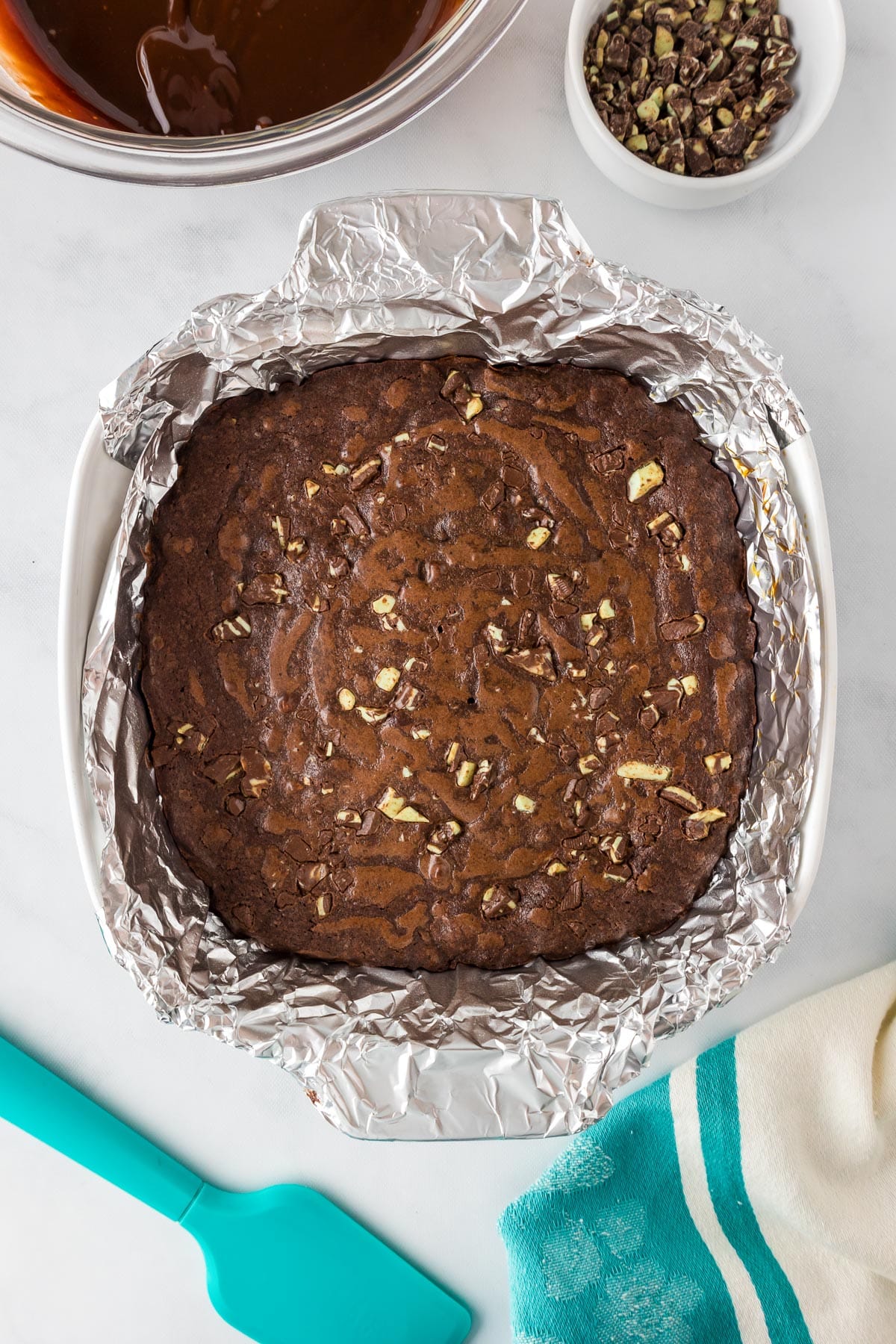 A square baking dish lined with aluminum foil is filled with Andes mint brownies after baking.