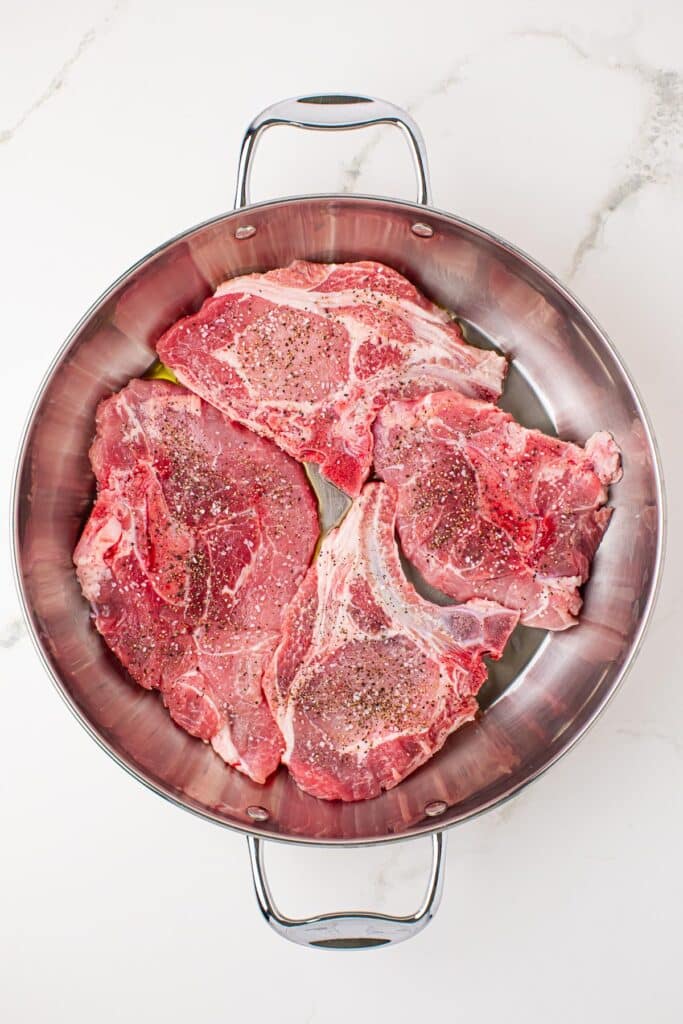 Four raw, seasoned porkchops in a large skillet.