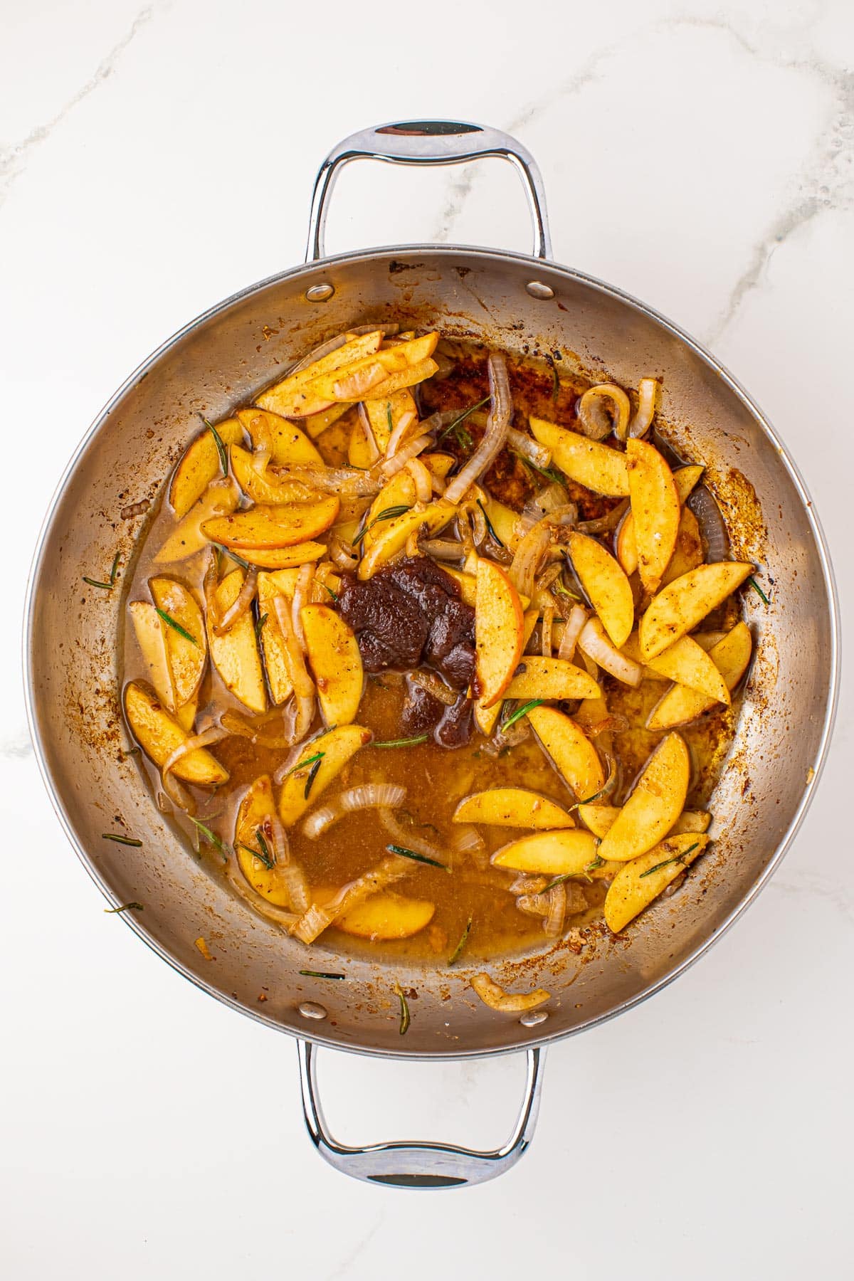 A skillet containing cooked apple slices, onions, chicken broth and apple butter.