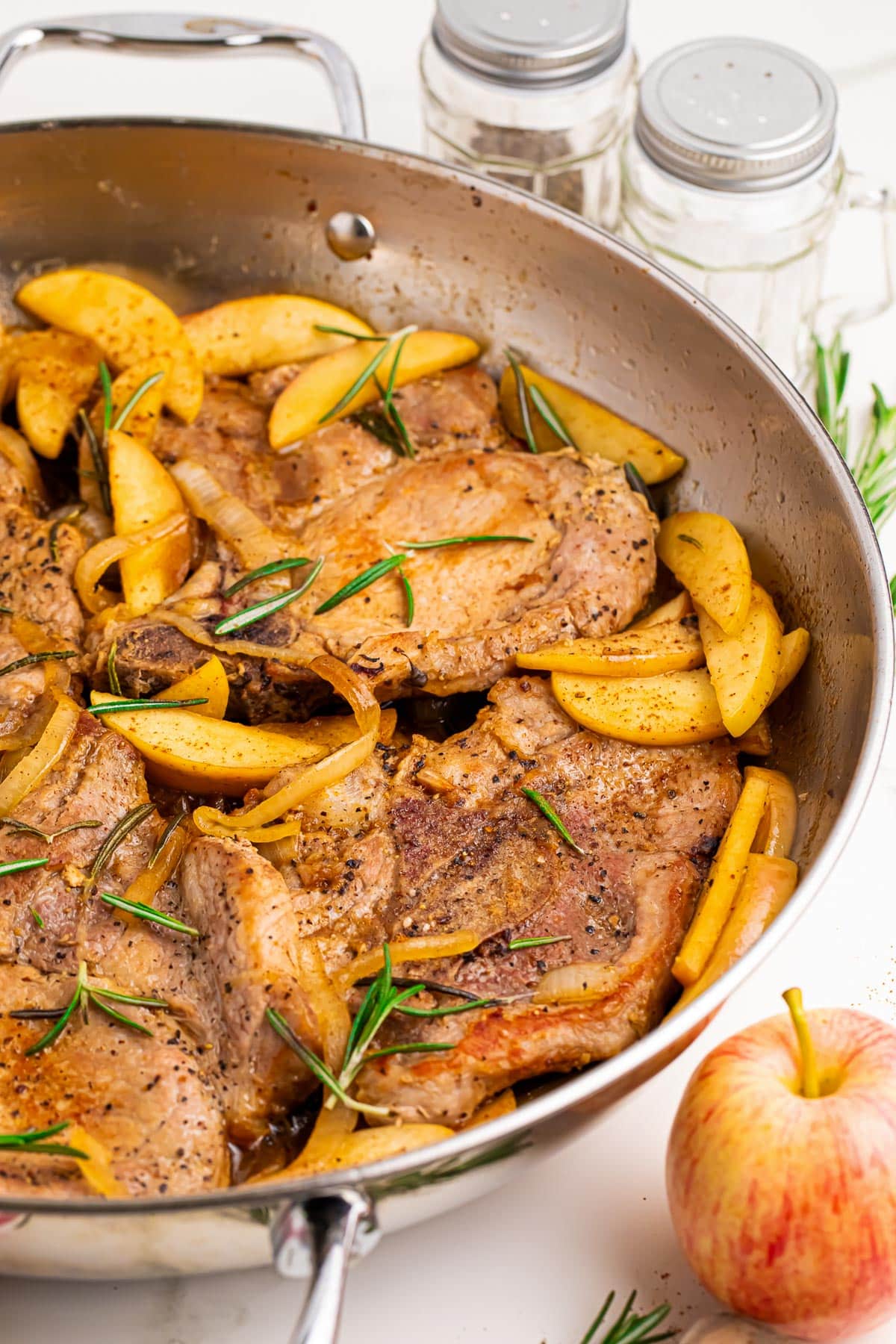 A skillet from the side containing browned porkchops and cooked apples with a apple butter pan sauce.