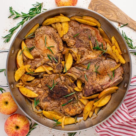 Pan-seared pork chops with apple butter and cooked apples, garnished with rosemary in a large skillet.