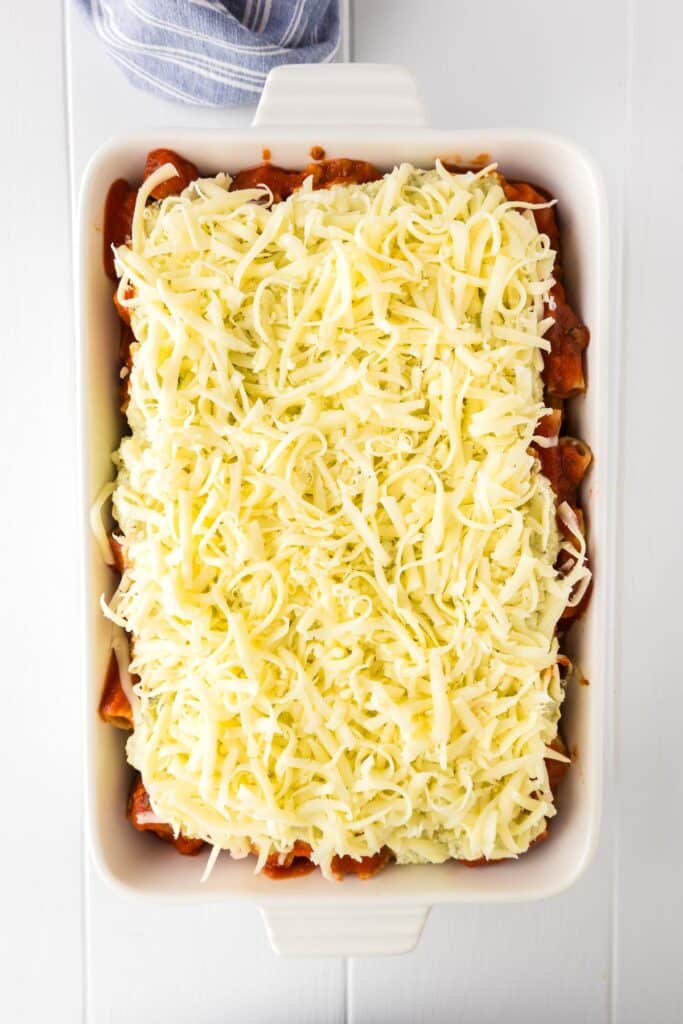 A rectangular baking dish filled with an unbaked rigatoni with chicken topped with shredded mozzarella cheese.