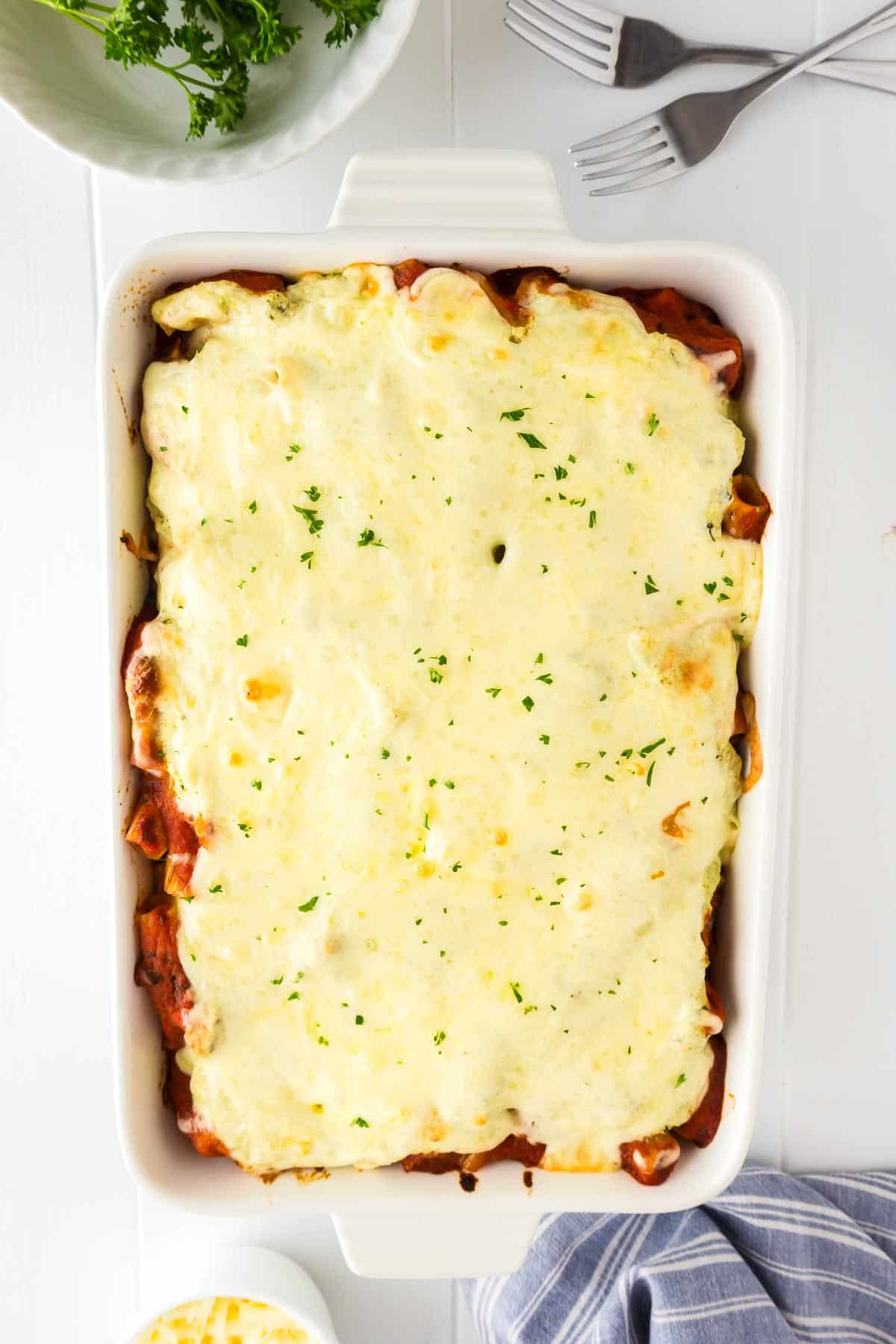 A white rectangular baking dish filled with baked rigatoni, topped with melted cheese.