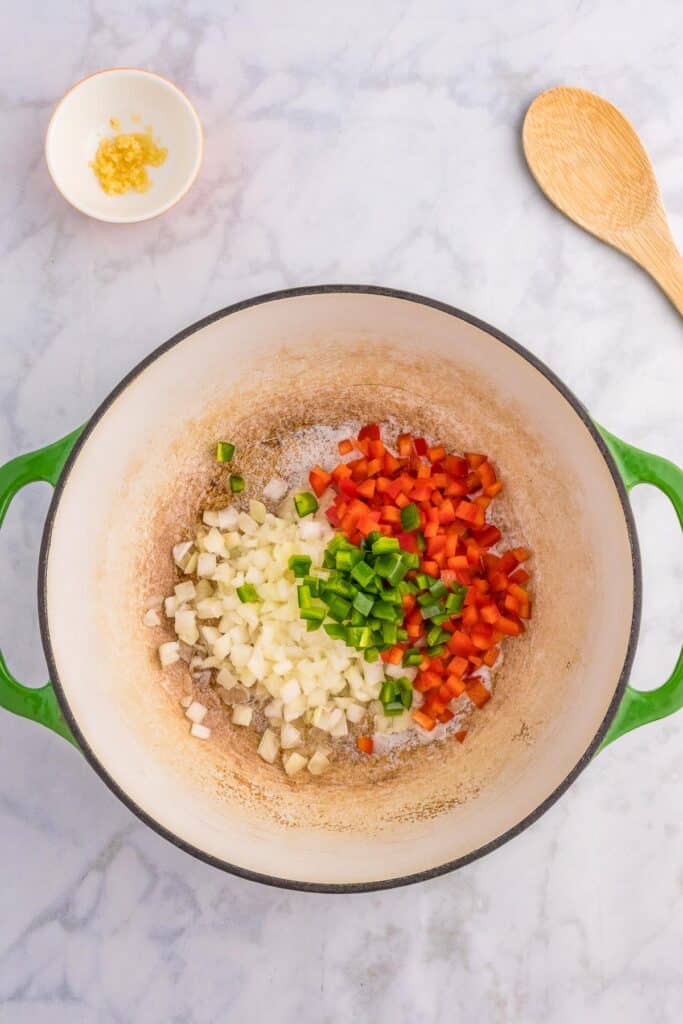 A large pot full of diced onion, bell pepper and jalapeno with minced garlic in a bowl nearby.